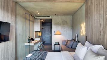 A modern hotel room with a large bed, a desk with a laptop, a chair, a small table, and a sofa.