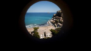 A coastal view through a circular window, featuring a beach, ocean, and buildings on a cliff. - Apartment Coblanca 16 (Benidorm)