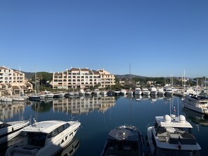 A marina with multiple yachts docked, a large building with balconies, and a clear blue sky.