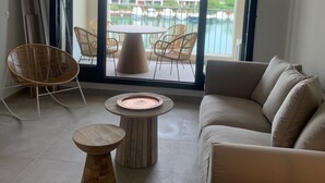 Un balcon spacieux offrant une vue sur un bâtiment d’hôtel et une piscine. On y trouve des chaises en osier, une table ronde en bois et un canapé beige.