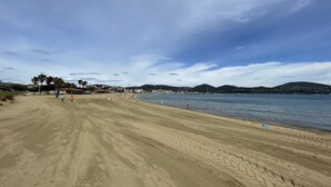 Une vaste plage de sable parsemée d’empreintes, une mer calme et des collines qui se dessinent à l’horizon.