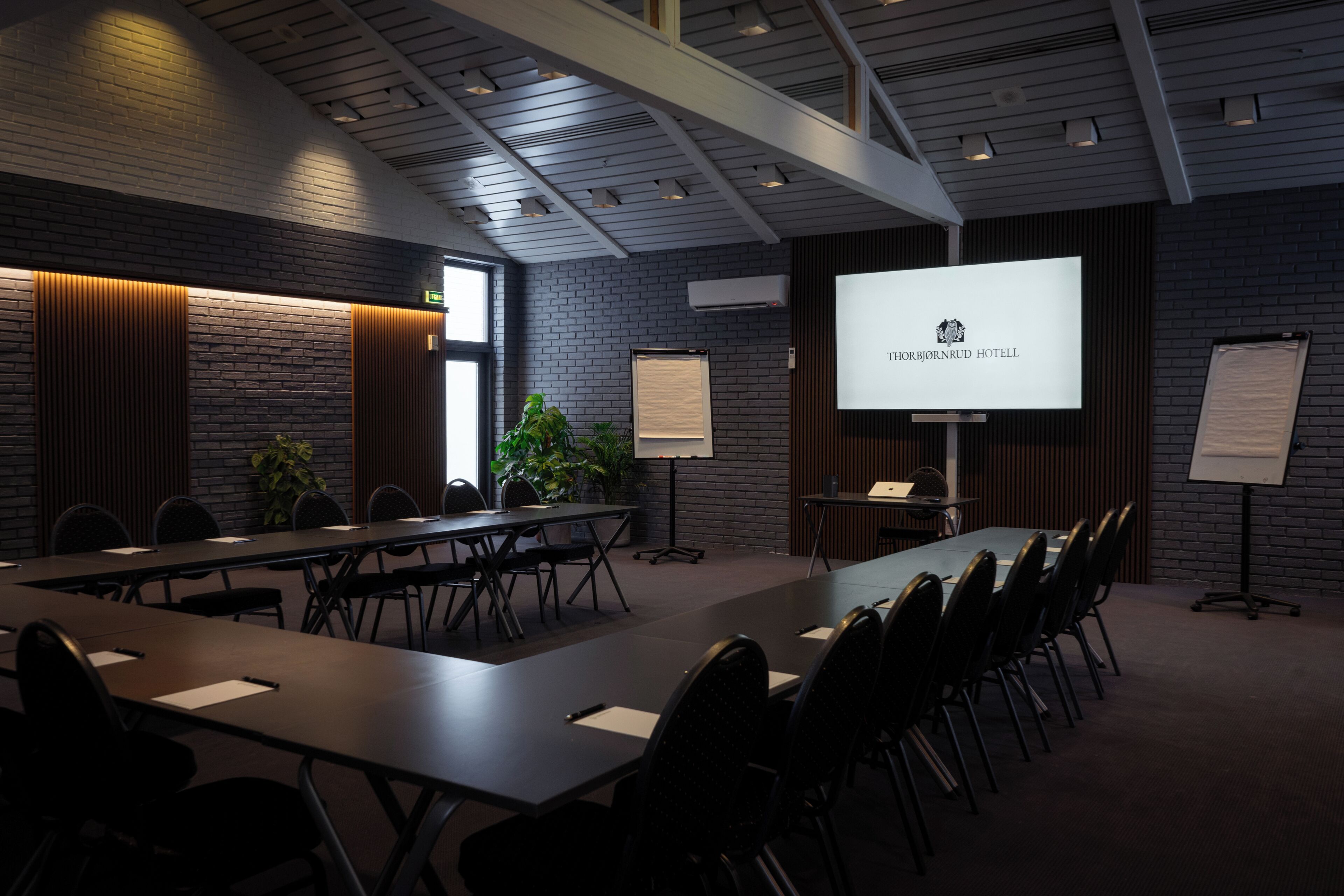 A conference room with a long table, chairs, a projector screen displaying 'THORHEIDENBRUD HOTEL', and a whiteboard.