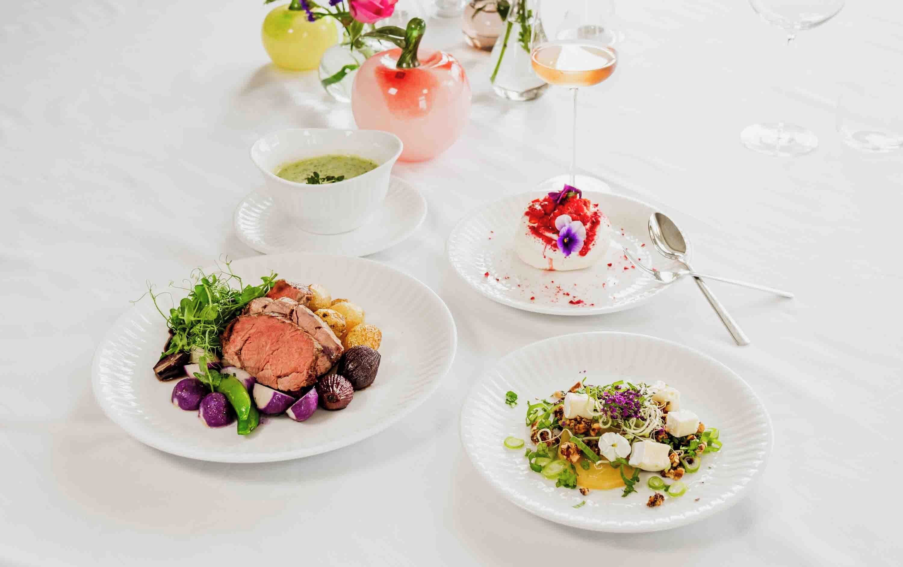 Et bord med tre tallerkener mad, en lille skål sauce og en pink vase med blomster.