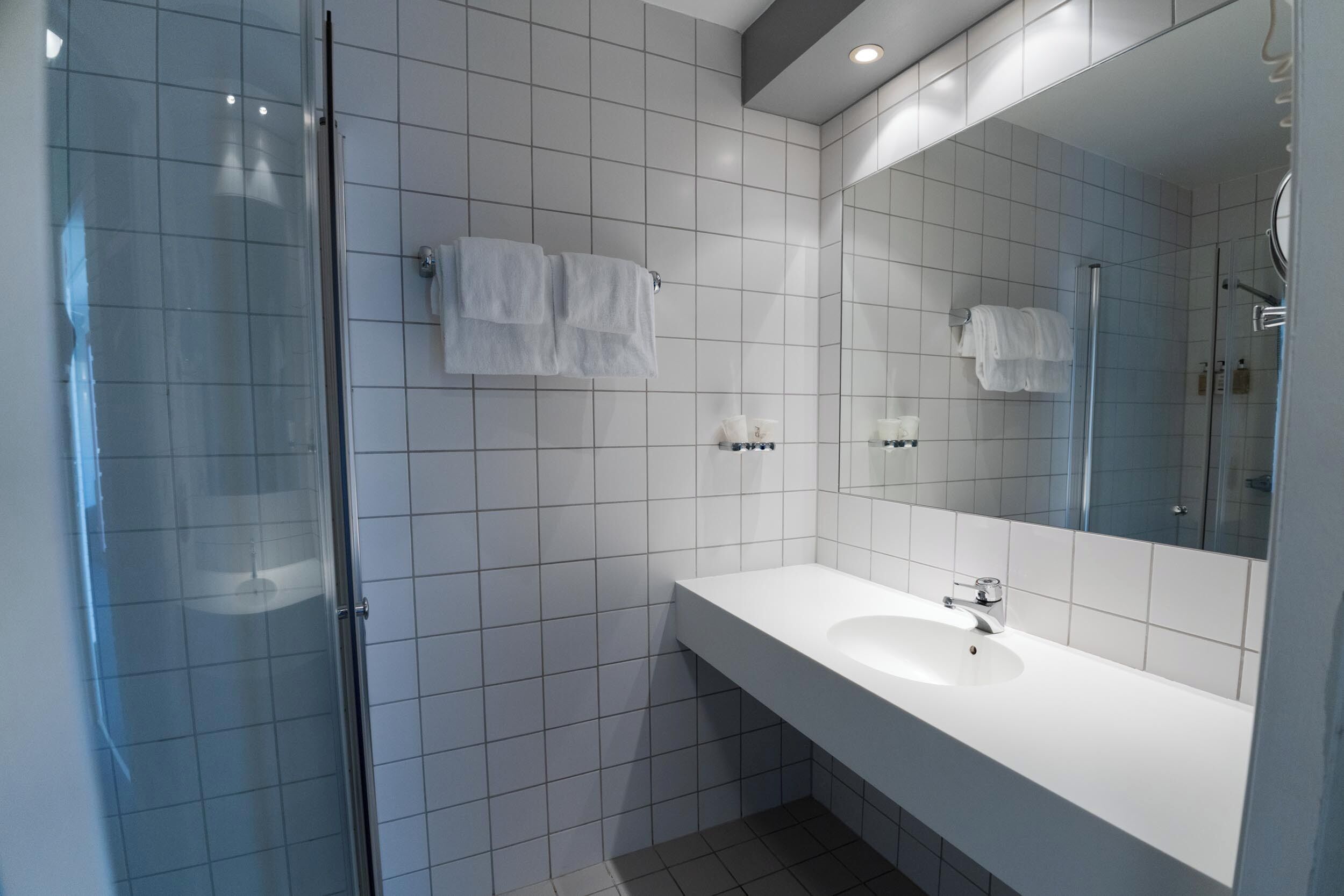 Un baño moderno con cabina de ducha de vidrio, un lavamanos blanco y un espejo grande.