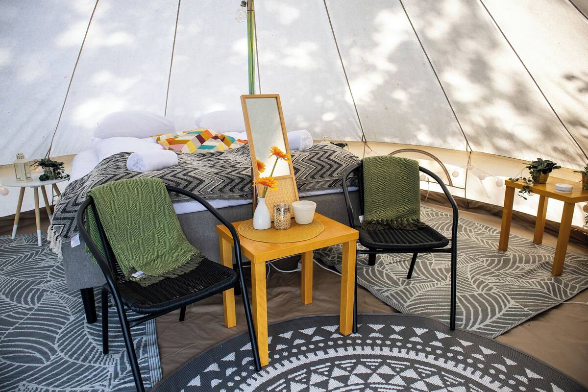 A tented accommodation with a bed, chairs, a table, and a mirror.