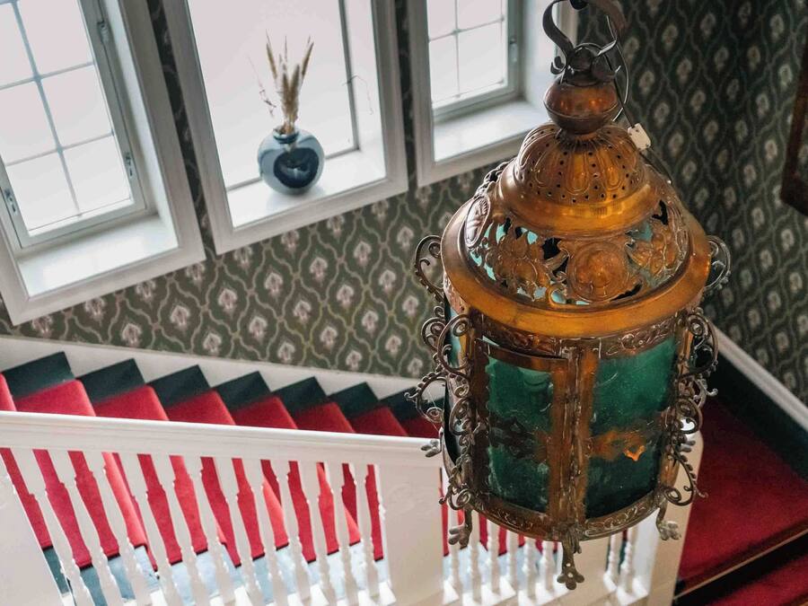 A staircase with red and white railings, a patterned wall, and a hanging lantern.