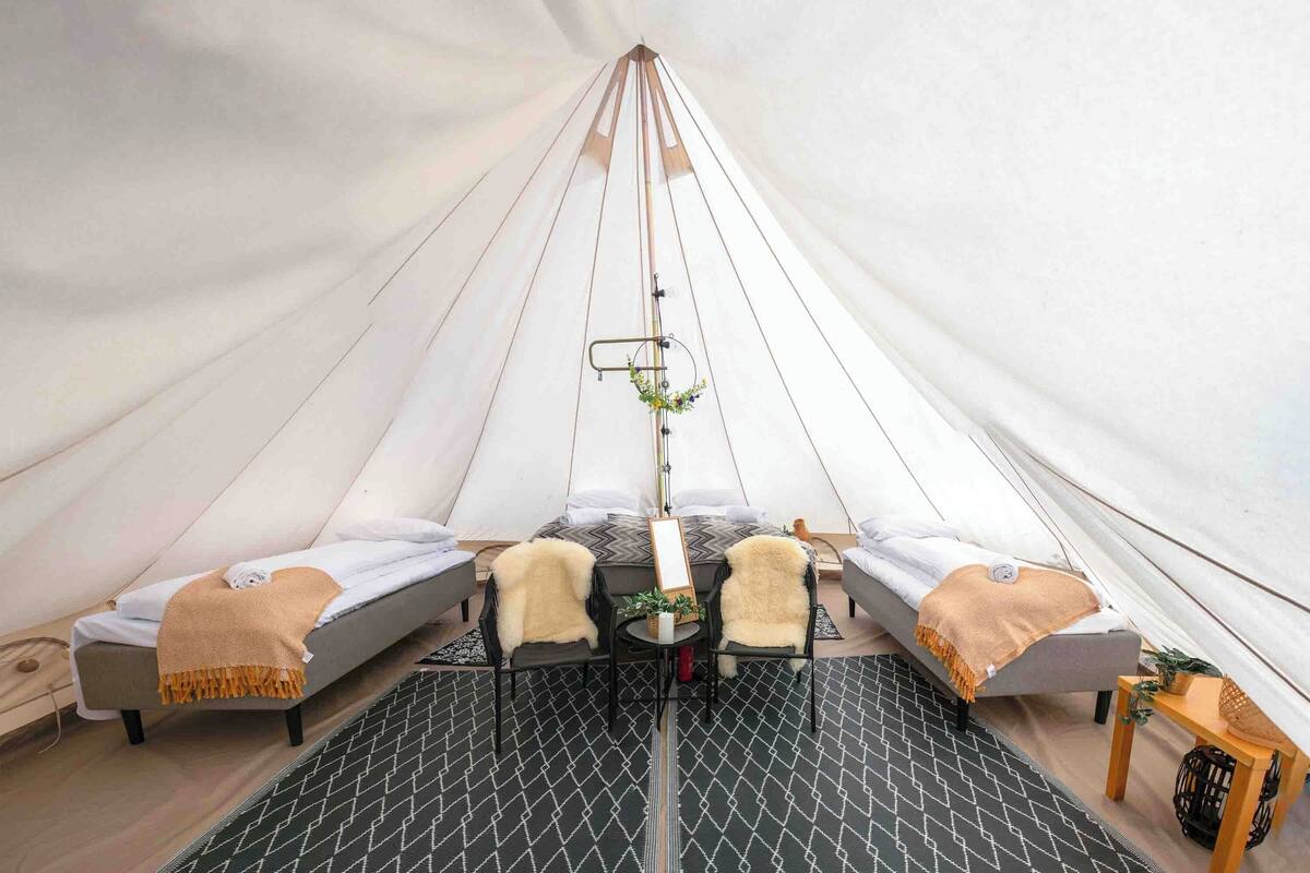 A tent with two beds, a small table, and a hanging light fixture.