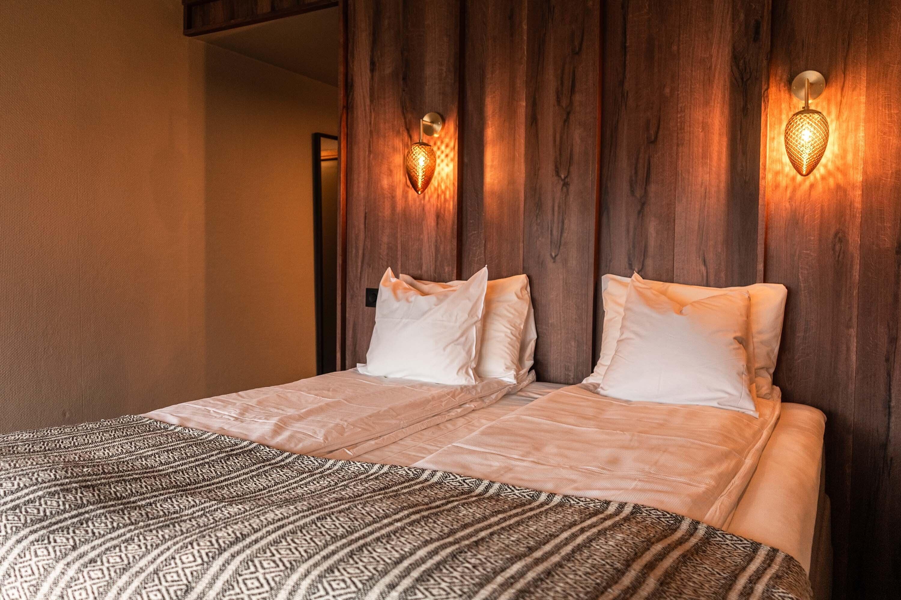A double bed with patterned bedding, wooden headboard, and wall-mounted light fixtures.