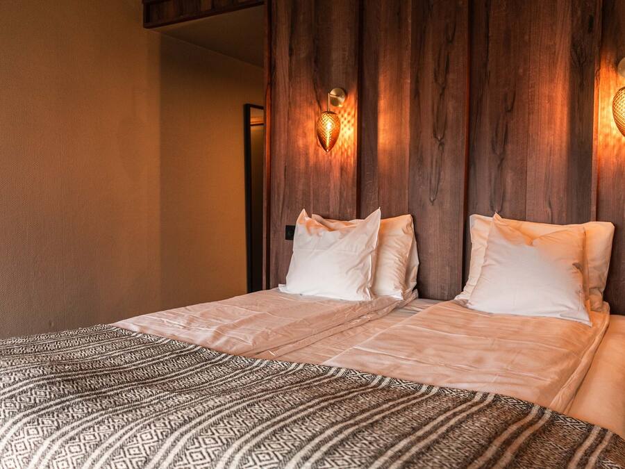 A double bed with patterned bedding, wooden headboard, and wall-mounted light fixtures.