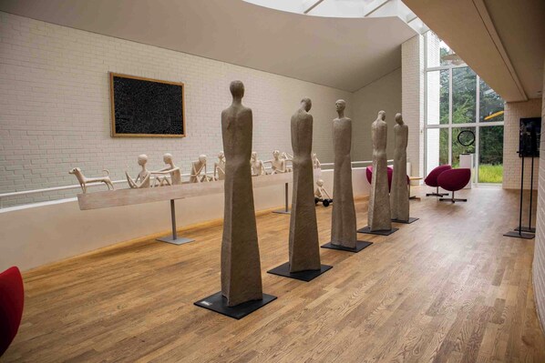 A modern art gallery with sculptures on display, a white brick wall, and large windows. - Thorbjørnrud Hotell (Jevnaker)