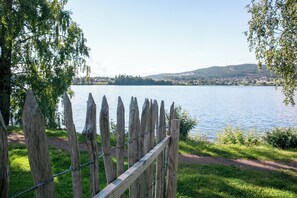 A wooden fence with a metal wire, a grassy area, and a lake with a distant town and hills. - Thorbjørnrud Hotell (Jevnaker)