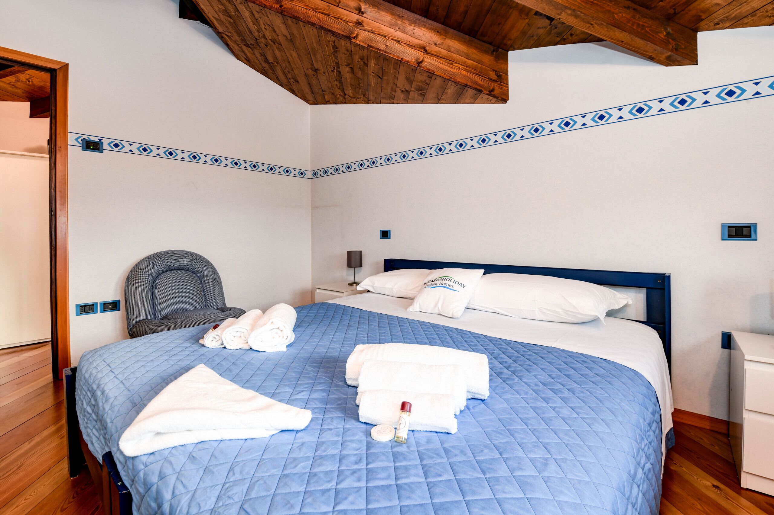 Una cama bien hecha con ropa de cama azul, almohadas blancas y toallas.