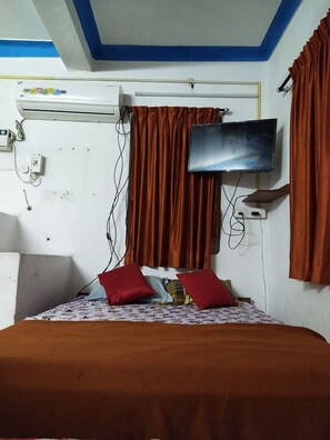 Ein Zimmer mit einem Bett, einem an der Wand befestigten Fernseher und einem Deckenventilator.