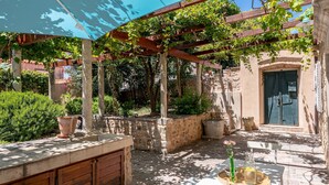 An outdoor patio with a pergola, stone walls, a table with a vase and bottle, and a door. - Hedera Estate, House Hedera VI (Dubrovnik)