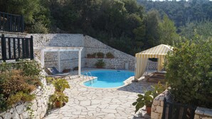 A stone pool surrounded by a stone wall, with a pergola and a covered seating area. - Villa Kalamos (Σύβοτα Λευκάδας)