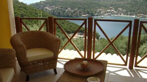 A wicker chair and a small table with a candle on a balcony overlooking a lake and buildings. - Villa Kalamos (Σύβοτα Λευκάδας)