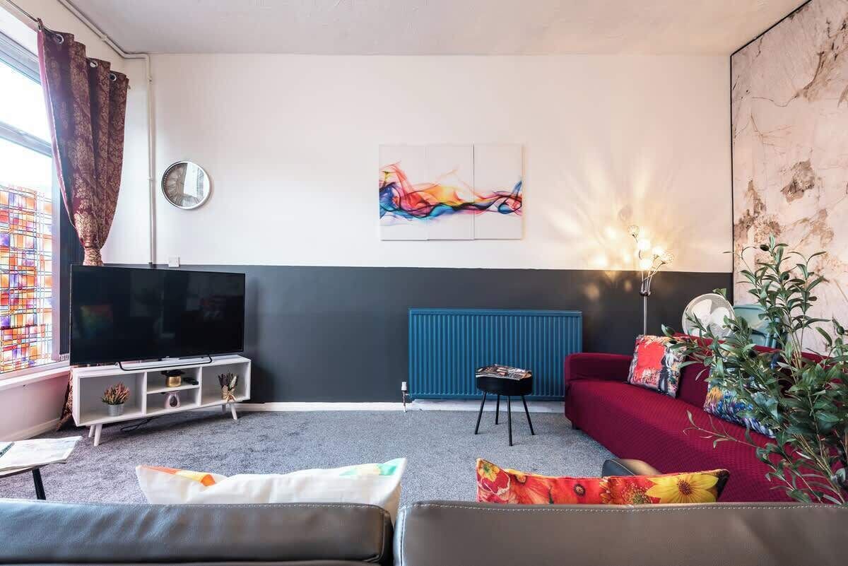A living room with a flat-screen TV, a red sofa, a coffee table, and a wall-mounted abstract painting.