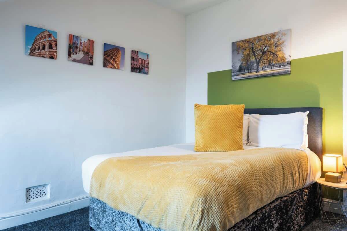 A hotel room with a bed, a nightstand, a lamp, and four wall-mounted pictures.
