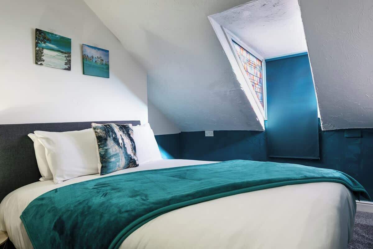 A bedroom with a bed, a window, and two paintings on the wall.