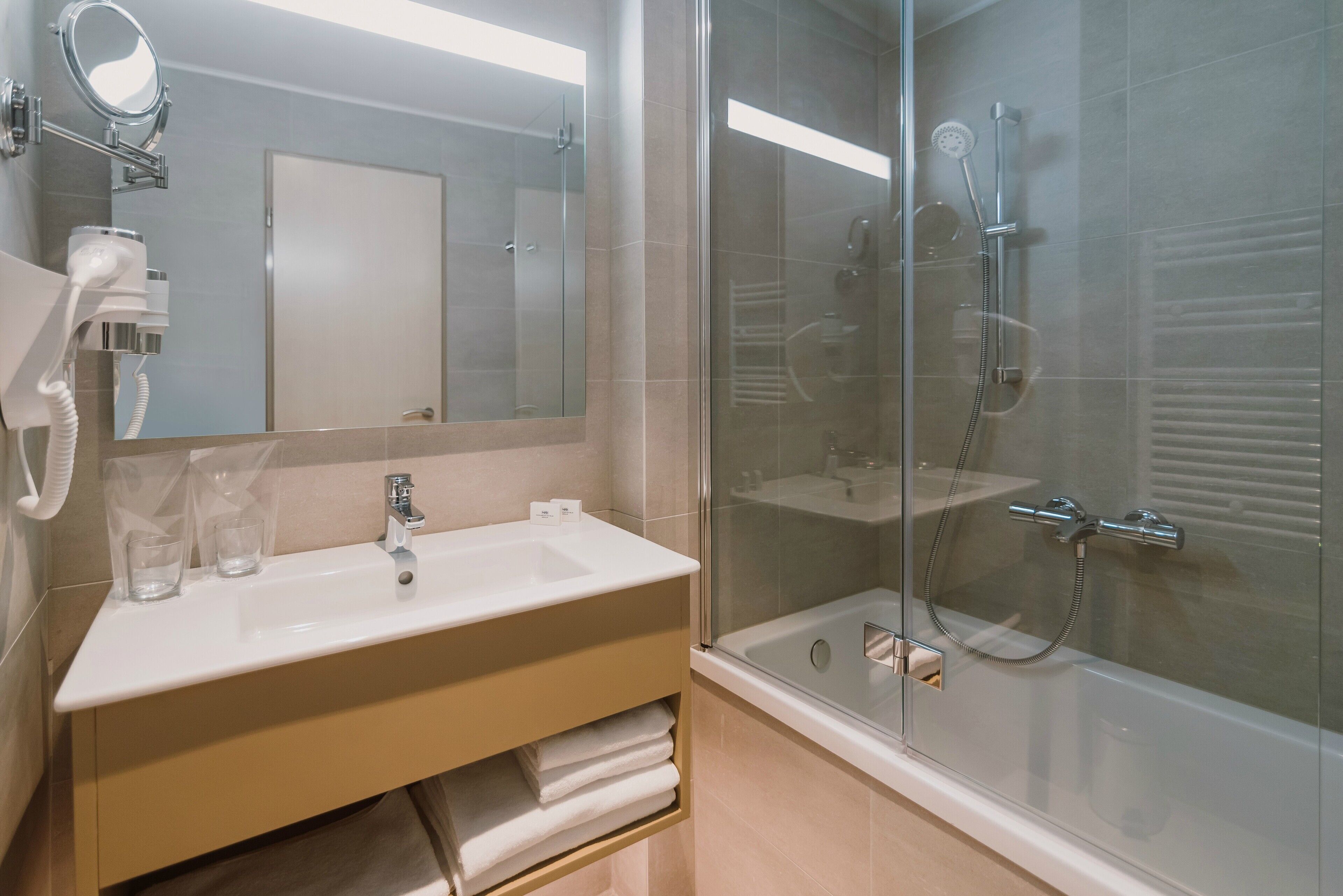 Un baño moderno con ducha envuelta en vidrio, un lavabo blanco y un espejo sobre él.