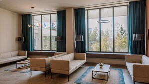 Una sala de estar amplia con un conjunto de sofás, una mesa de centro y ventanas grandes con cortinas.