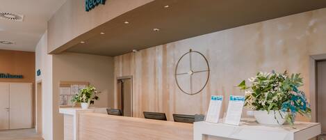 A reception area with a wooden reception desk, a clock, and potted plants.