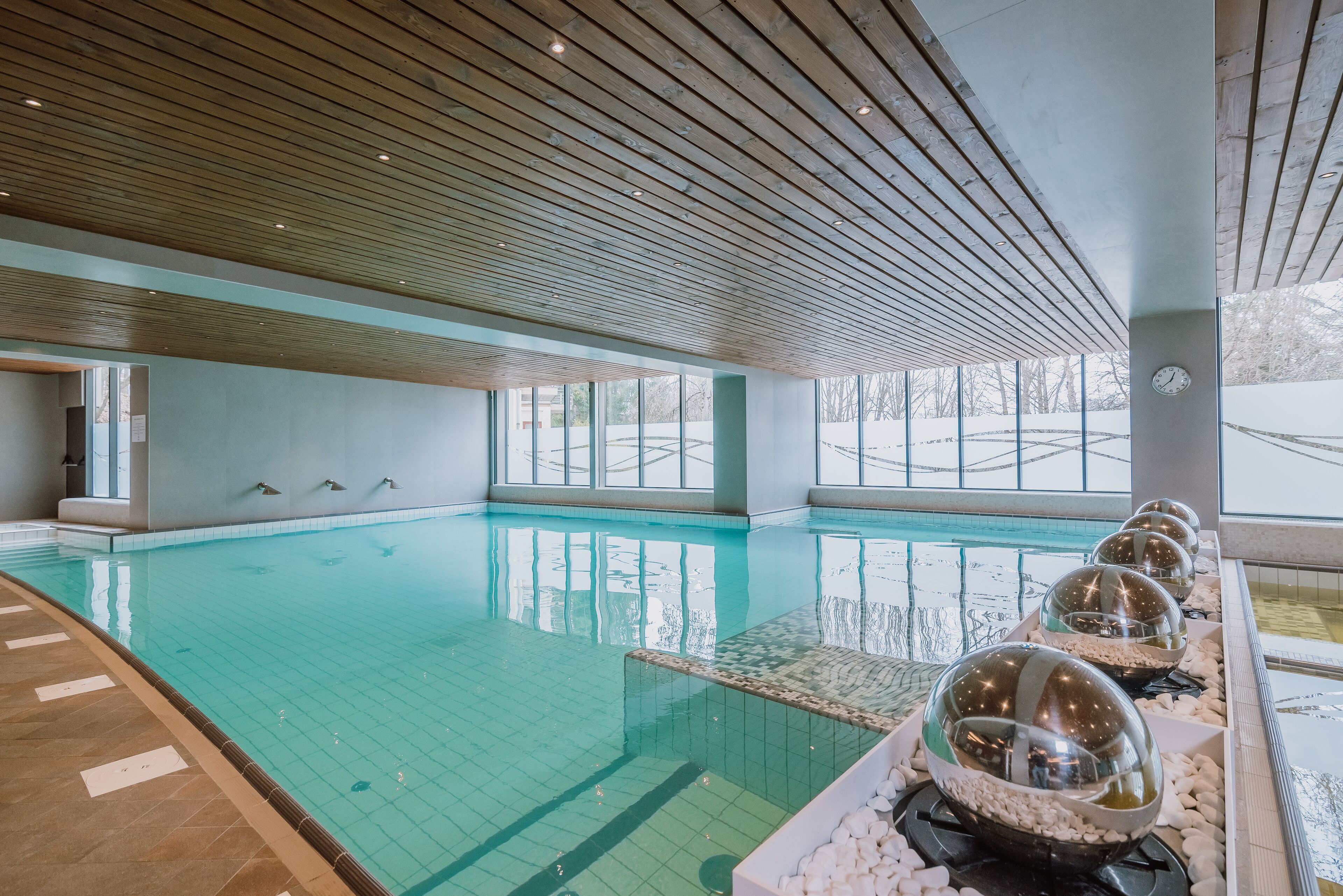 An indoor swimming pool with clear water, wooden ceiling, and large windows.