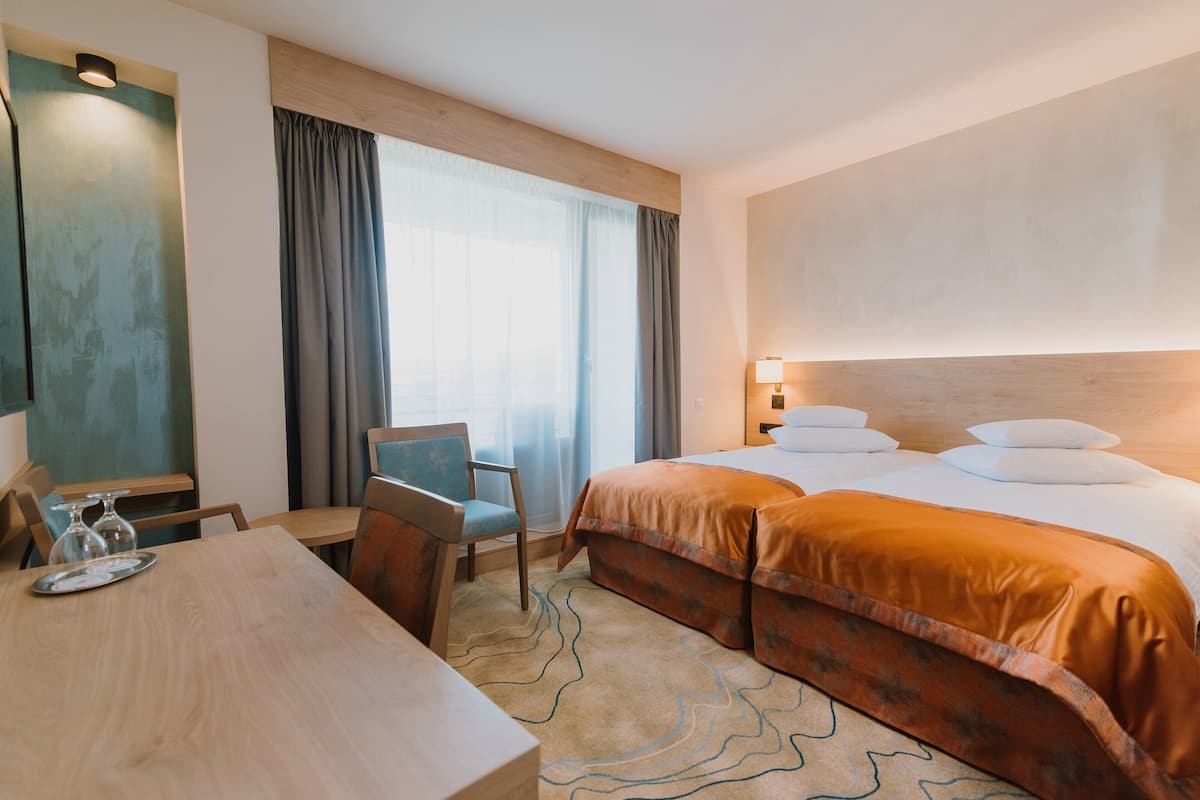 Una habitación de hotel con cama, escritorio, silla y ventana con cortinas.