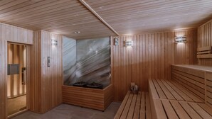 Una sauna de madera con bancos, un baño de vapor con paredes de vidrio y luces fijadas a la pared.