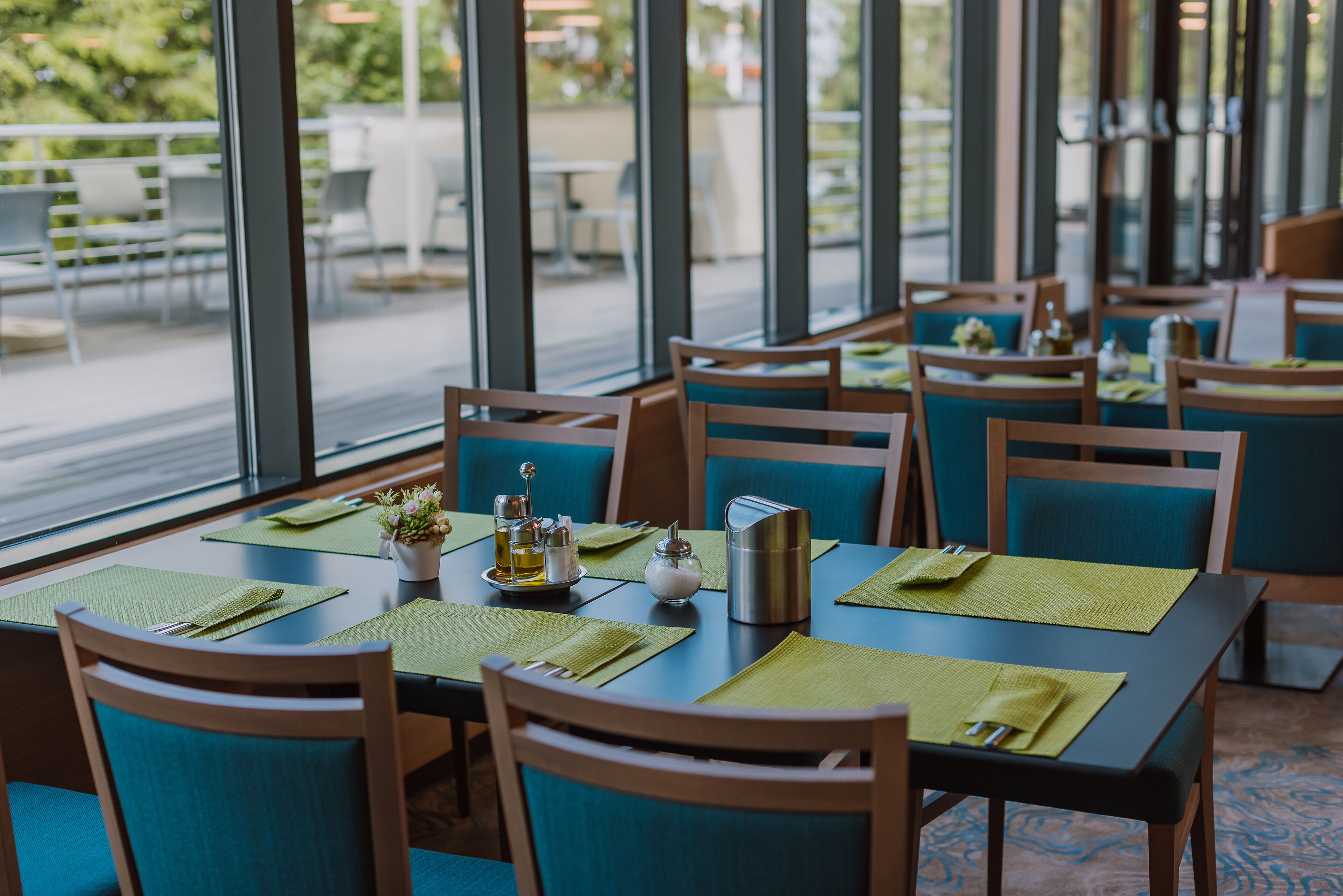 An indoor dining area with tables set for two, featuring green placemats and wooden chairs.