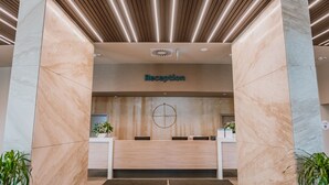 Un área de recepción con un mostrador de mármol, un adorno circular en la pared e iluminación lineal en el techo.