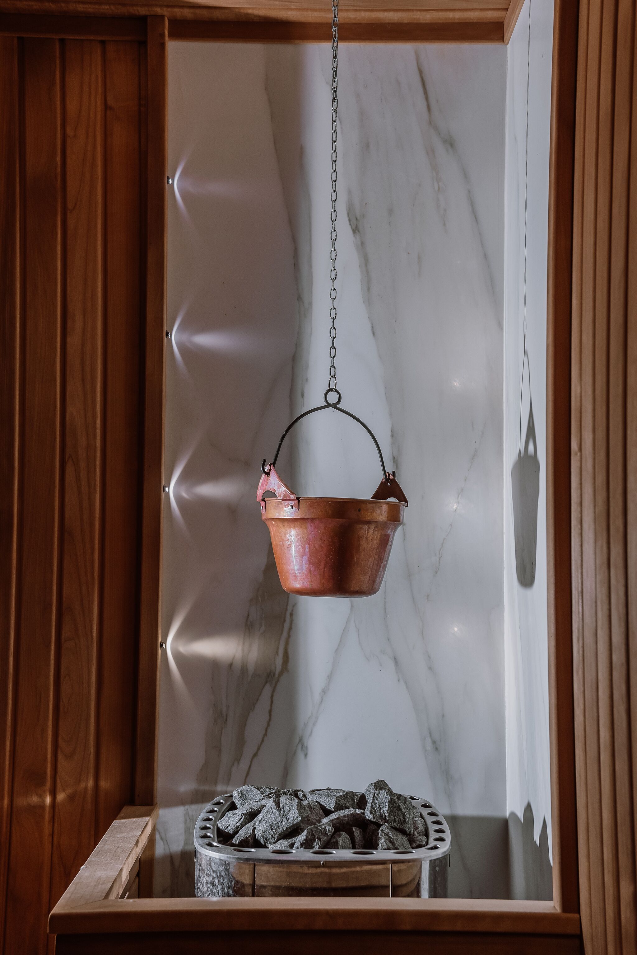 Een koperen pot hangt aan een ketting boven een open haard met een stenen vuurkamer eronder.