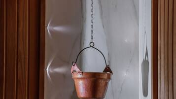 Een koperen pot hangt aan een ketting boven een open haard met een stenen vuurkamer eronder.