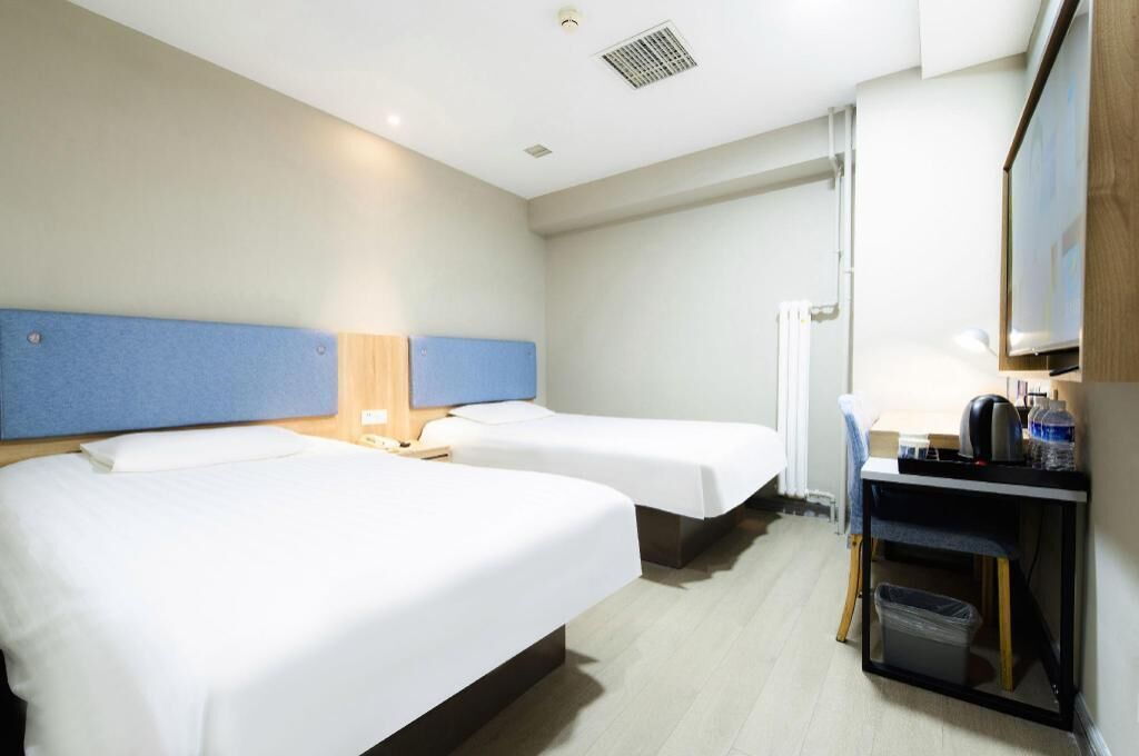 Habitació d'hotel amb dos llits individuals, un escriptori petit amb una cadira, un gresol i un televisor fixat a la paret.