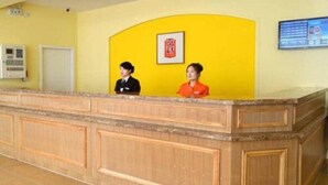 A reception desk with two staff members, a yellow wall, a framed picture, and a digital display. - Home Inn Hotel Beijing West North Plaza (Beijing)