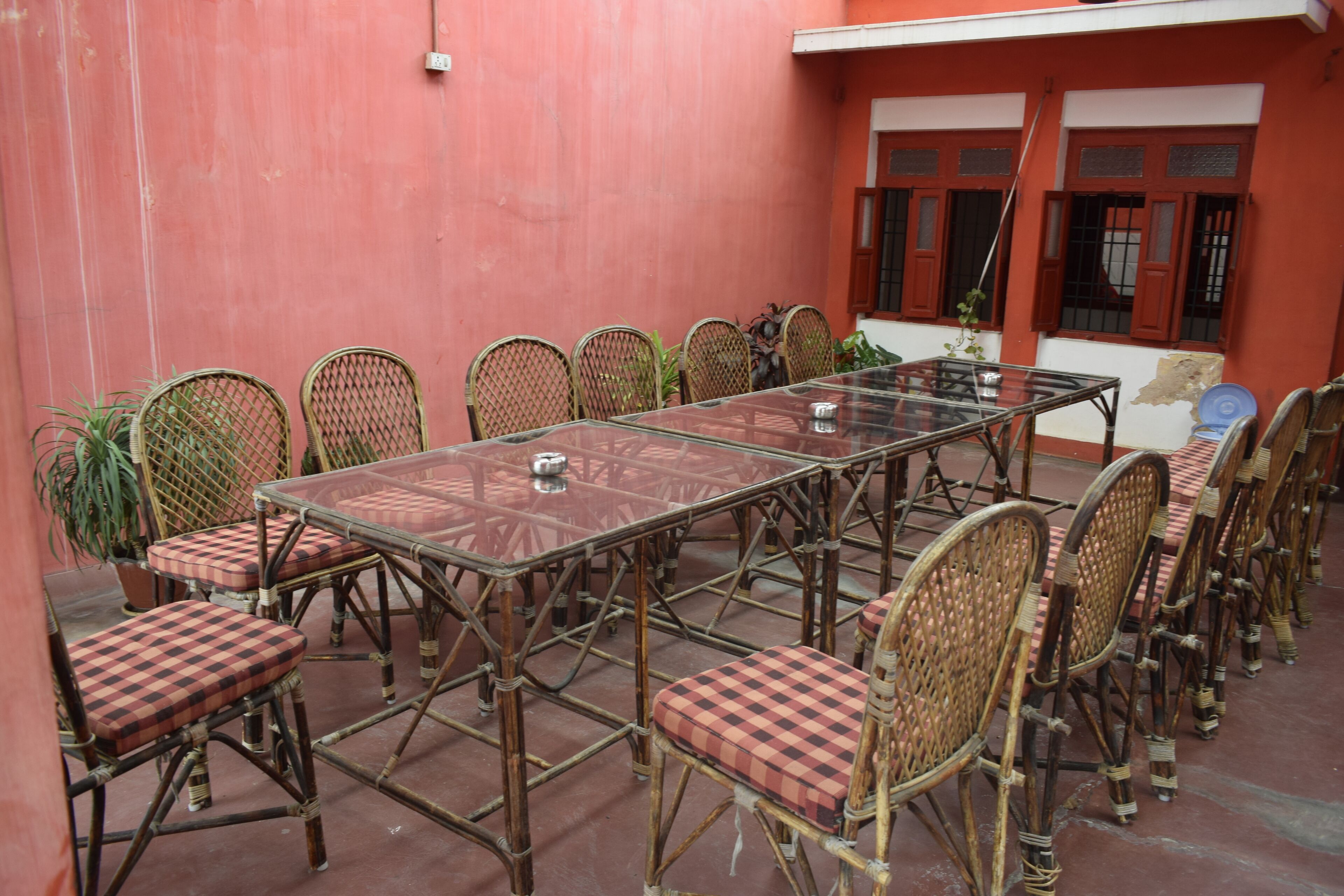 A meeting room with a glass table and wicker chairs, a potted plant, and a red wall.