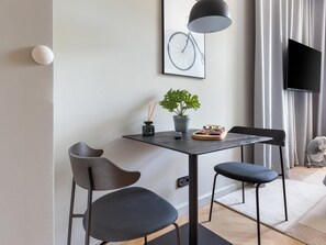 A modern room with a table, two chairs, a potted plant, a remote control, and a mounted TV.