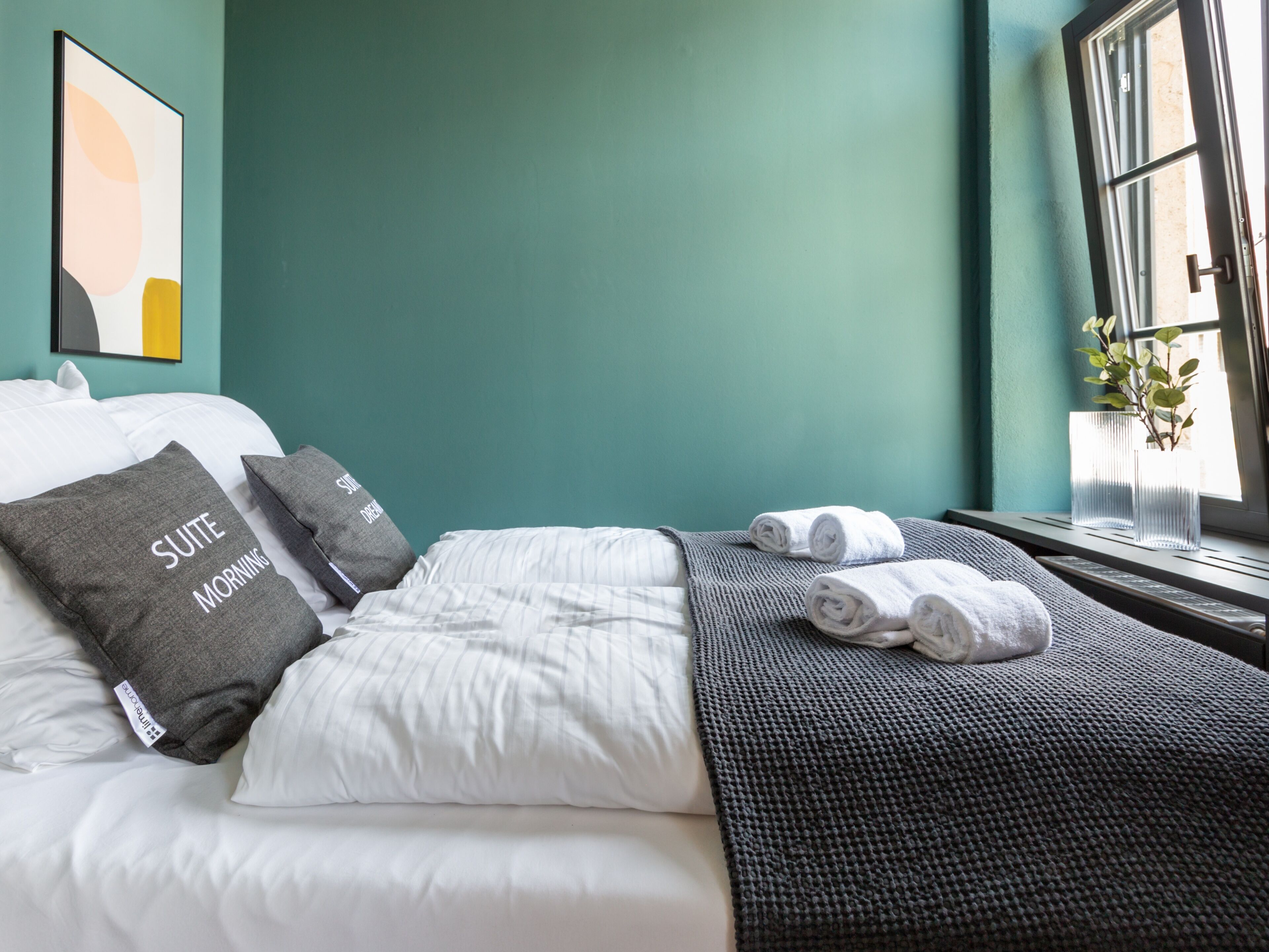 Habitación de hotel con cama, almohadas, una manta y ventana con planta.