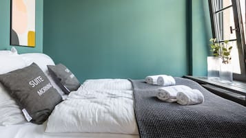Habitación de hotel con cama, almohadas, una manta y ventana con planta.