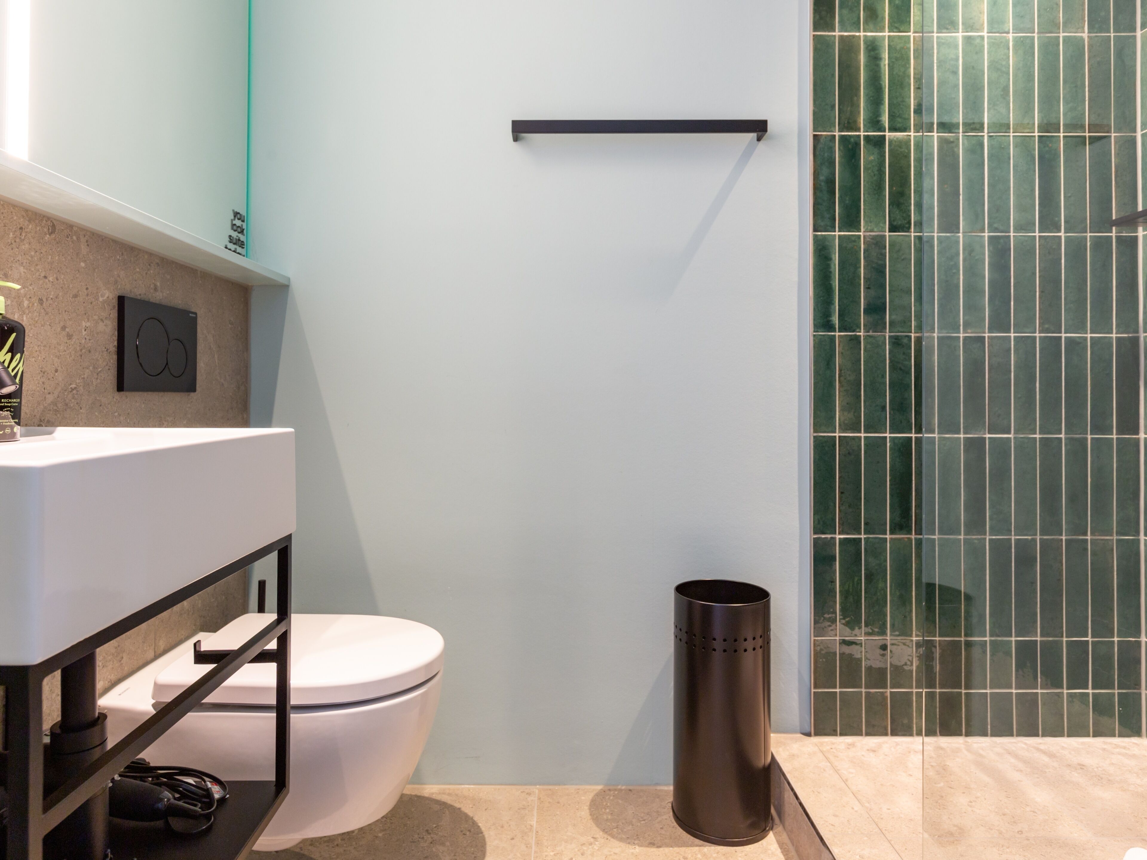 A modern bathroom with a white toilet, a black trash bin, and a glass shower enclosure.