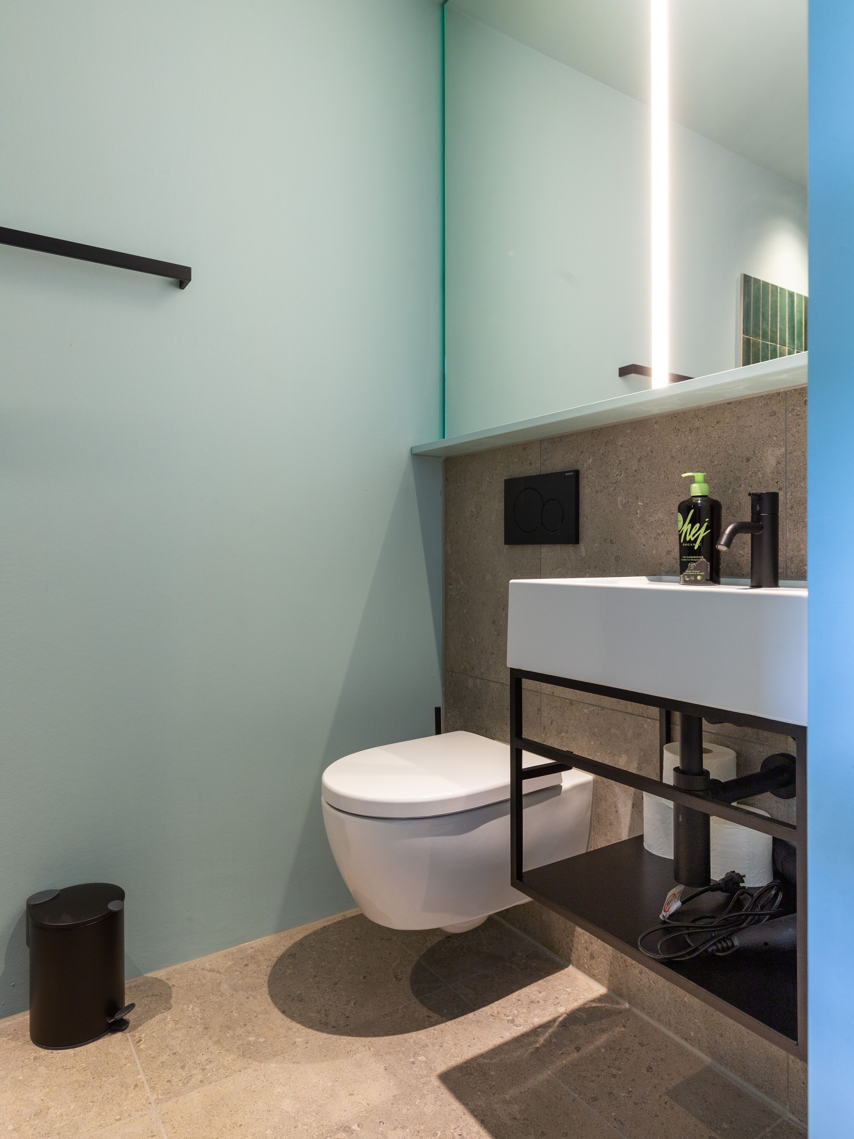Un baño moderno con un inodoro blanco, un lavabo negro y un espejo sobre el lavabo.