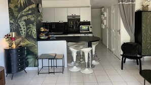 Uma cozinha moderna com armários brancos, bancada preta e uma área de refeições com cadeiras brancas.