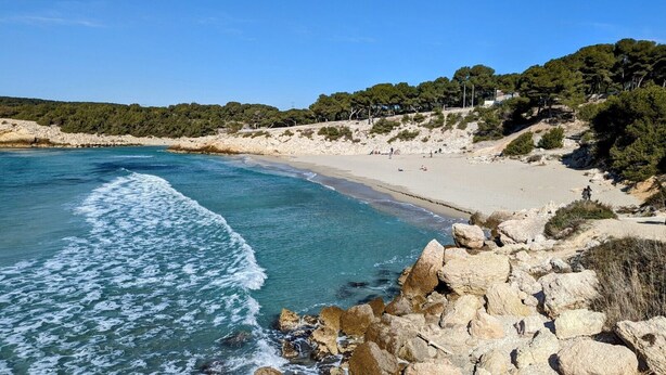 Uma praia costeira com terreno rochoso e faixa de areia.