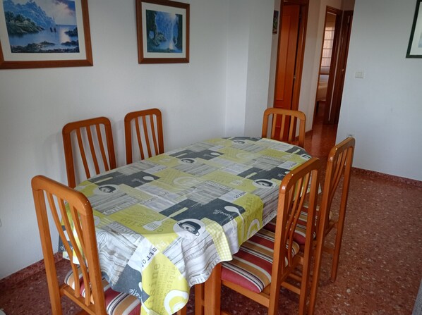 A dining area with a table covered by a patterned tablecloth, surrounded by wooden chairs with striped cushions.