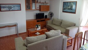 A living room with a sofa, a television, a fan, and a painting on the wall. - CANCUN VII 6º,  Solo Familias! (Playa de Gandía)