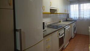 A compact kitchen with a refrigerator, microwave, oven, and washing machine. - CANCUN VII 6º,  Solo Familias! (Playa de Gandía)