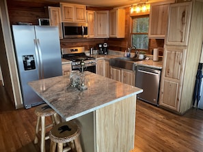 Une cuisine moderne avec des meubles en bois, des appareils en acier inoxydable, un plan de travail en granit et un petit îlot central avec des tabourets.