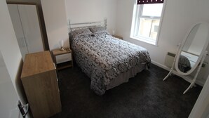 Een slaapkamer met een bed, een houten dressoir, een nachtkastje, een spiegel en een raam met uitzicht.
