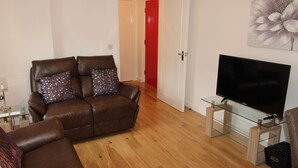 Een woonkamer met een bruine leren bank, een glazen salontafel en een flatscreen televisie op een glazen voet.