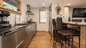 Una cocina moderna con electrodomésticos de acero inoxidable, techo de madera y una barra con taburetes.